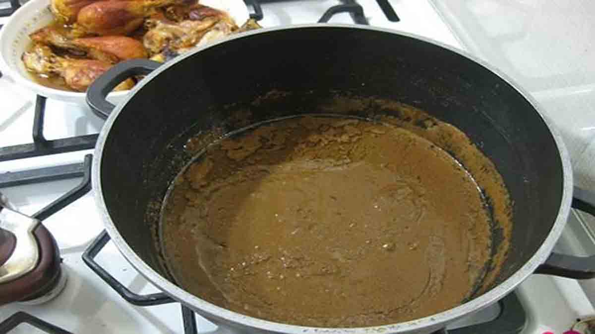 مرحله چهارم پخت فسنجون با مرغ و اضه کردن آب سرد یک قابلمه حاوی گردو روغن انداخته و آب که بر روی گاز قرار دارد و در پشت قابلمه تکه های مرغ سرخ شده در یک بشقاب قرار دارد و مرحله چهارم پخت فسنجون با مرغ را نشان می دهد