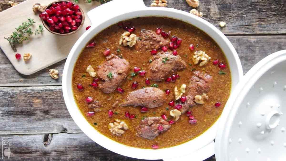 خورشت فسنجون با مرغ برای 4 نفر یک قابلمه حاوی خورشت فسنجون با مرغ که با دانه های انار و مغز گردو تزیین شده است و درب قابلمه در کنار آن قرار دارد و یک کاسه کوچک دانه انار در کنار قابلمه قرار دارد و بر روی میز کمی مغز گردو ریخته شده است