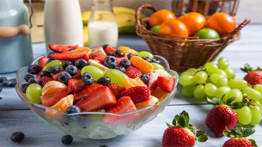 مواد غذایی مجاز در رژیم جنرال موتورز اصلی یک کاسه حاوی تکه های توت فرنگی، بلوبری، انگور و تکه های پرتقال در پشت کاسه یک سبد نارنگی و پرتقال، دو عدد موزو دو بطری شیر قرار دارد و در کنار کاسه میوه چهار عدد توت فرنگی و یک حوشه انگور ریخته شده است و به مواد غذایی مجاز در رژیم جنرال موتورز اشاره دارد