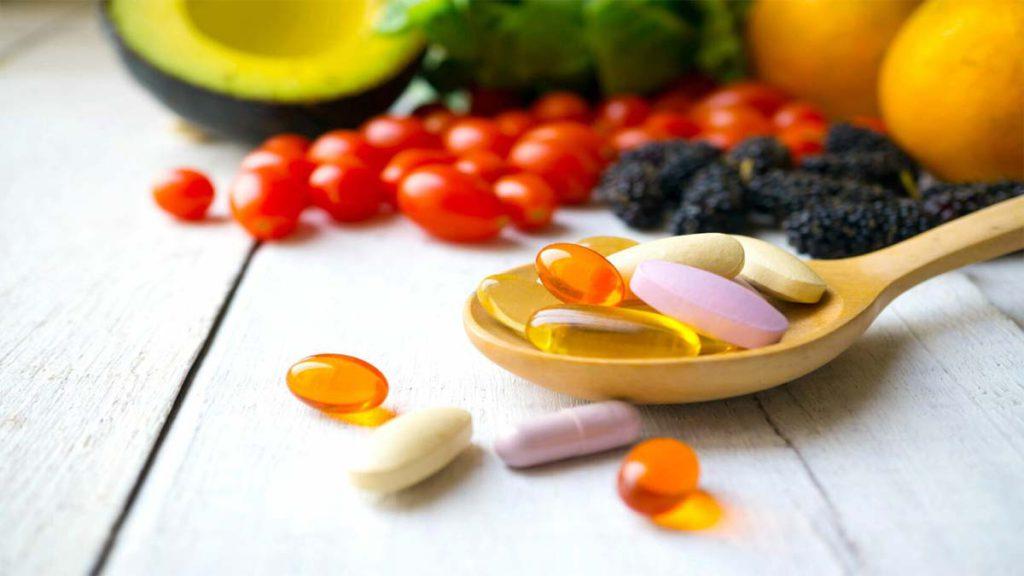 ویتامینها و مکملها در رژیم کتوژنیک رایگان یک قاشق حاوی قرص های ویتامین و مکملهای معدنی است و تصویر پشت قاشق تمشک، کاهو و گوجه فرنگی است که به عنوان میان وعده در رژیم کتوژنیک رایگان کاربرد دارد.