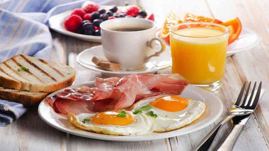 تصویر در بهترین رژیم لاغری یک ماهه یک صبحانه پر پروتئین را نشان می دهد که شامل تخم مرغ، گوشت، قهوه، آب پرتقال، تکه های پرتقال، بلوبری و تمشک است
