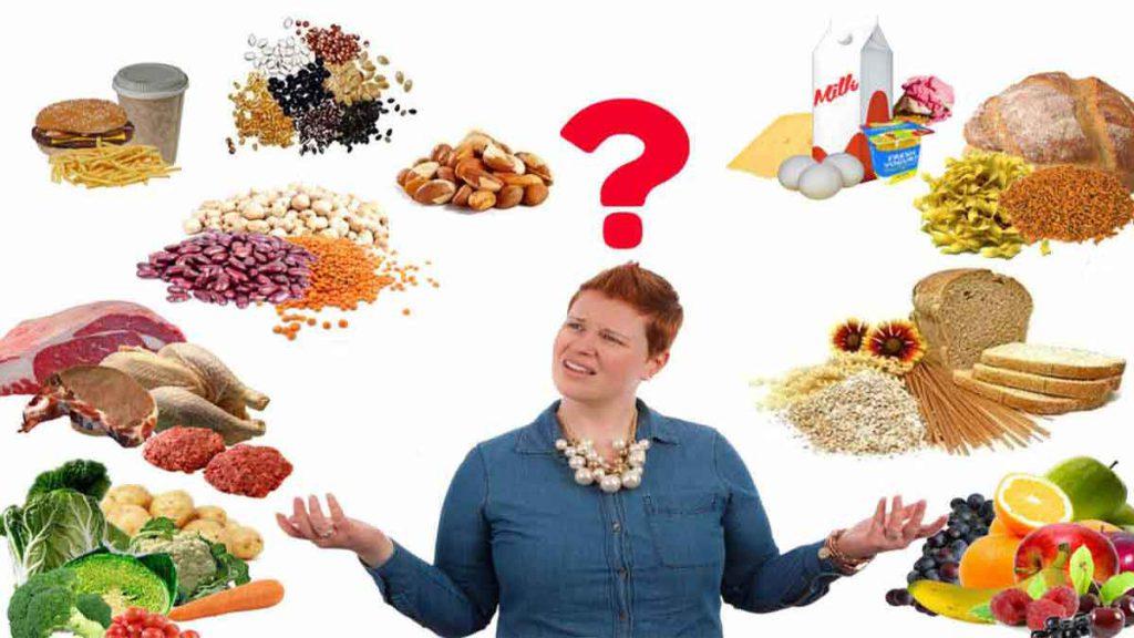 انتخاب بهترین رژیم لاغری یک خانم با اضافه وزن و انواعی از غذاهای مختلف مغزها، حبوبات، سبزیجات، میوه، تخم مرغ و... که در اطراف آن قرار دارد و برای انتخاب بهترین رژیم لاغری رایگان سوال دارد.