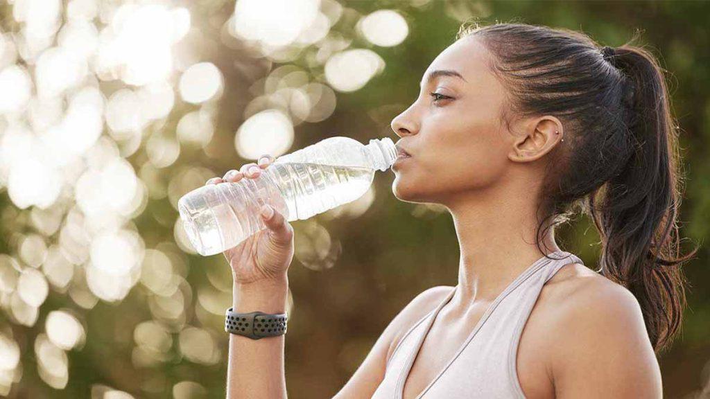 تصویر یک خانم در طبیعت را نشان می دهد که  بعد از ورزش با بطری آب می نوشد و معرف بهترین رژیم لاغری یک ماهه است.