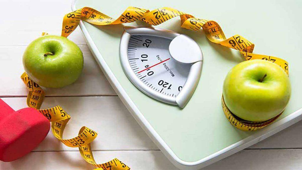 عکس حاوی ترازو، سیب سبز، وزنه و سانتی متر است که مرتبط با بهترین رژیم لاغری سریع است.