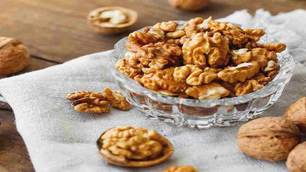 گردو و سازگاری فسنجون با مرغ و رژیم لاغری یک کاسه مغز گردو و تعدادی گردو پوست دار و مغز گردو که در اطراف کاسه ریخته شده اند و سازگار کردن خورشت فسنجون با مرغ را با رژیم لاغری نشان می دهد