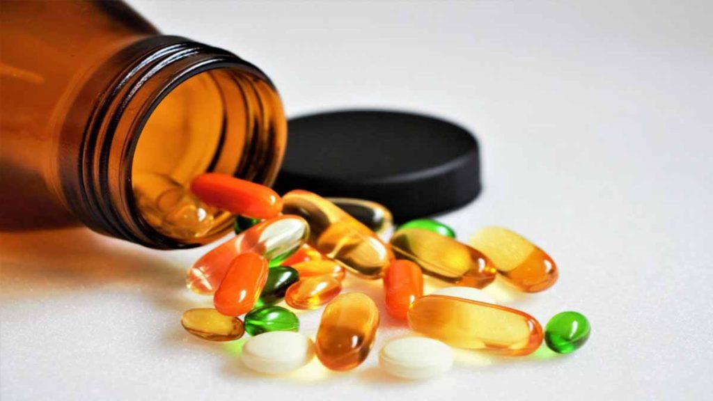 قرص های مکمل برای رژیم وگان یک شیشه حاوی قرص های ویتامین و مکمل های مورد نیاز برای رژیم وگان که قرص های بر روی زمین ریخته است